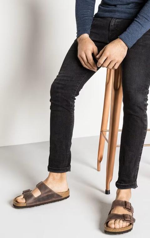 Uomo seduto su sgabello con sandali e jeans neri.